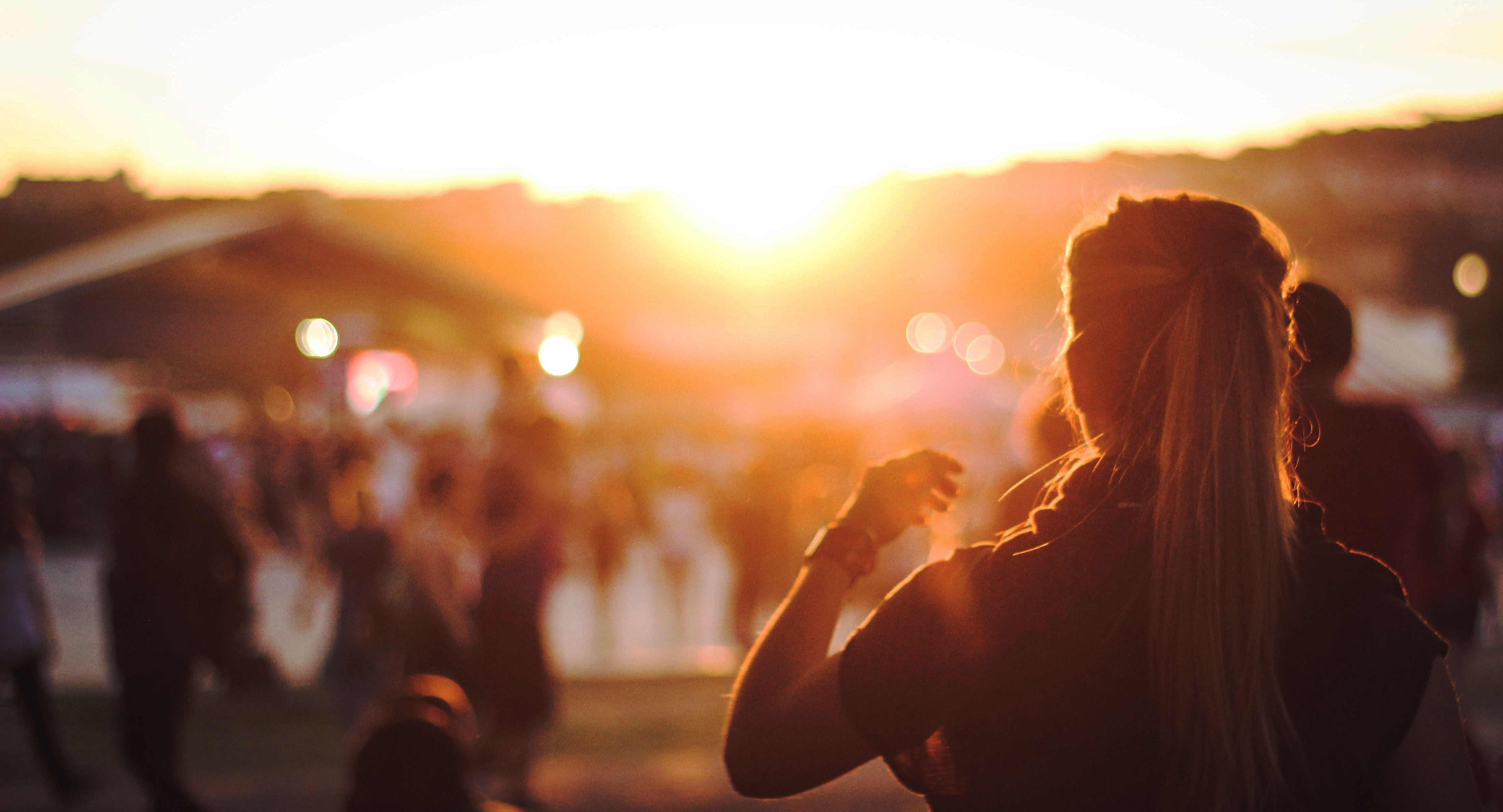 Bild på tjej som står med ryggen mot solnedgång och mycket folk i bakgrunden
