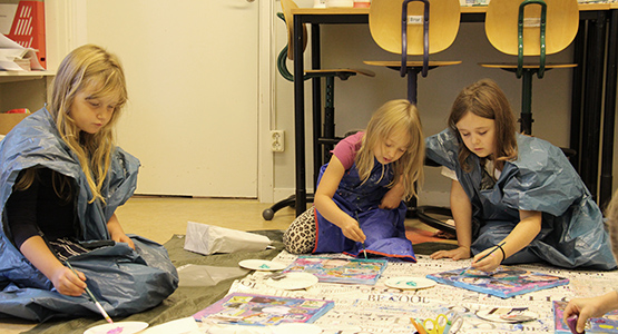 Två yngre flickor sitter på golvet och målar på en målarduk. 