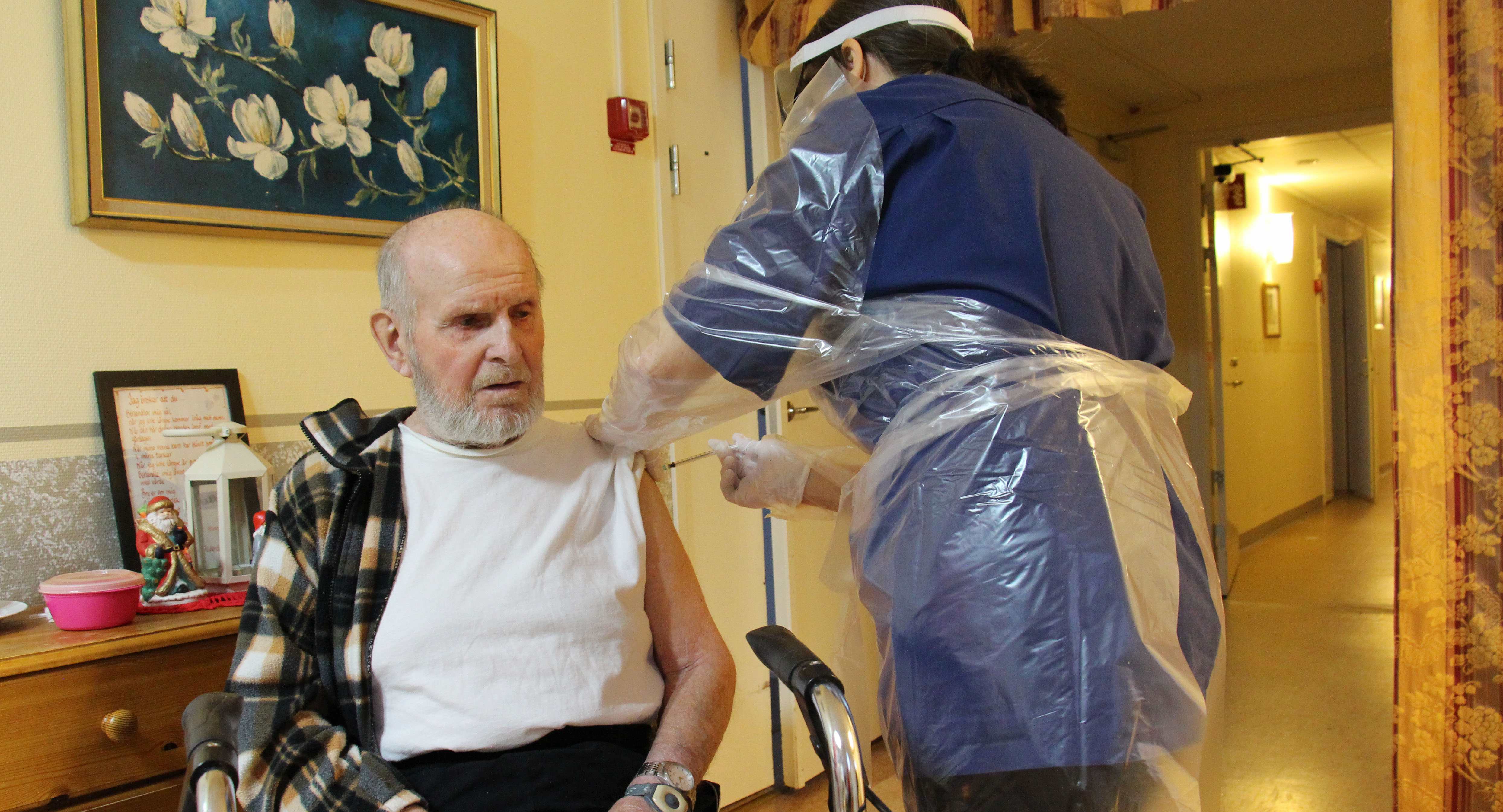 Äldre man får en spruta i armen av sköterska med skyddsutrustning.
