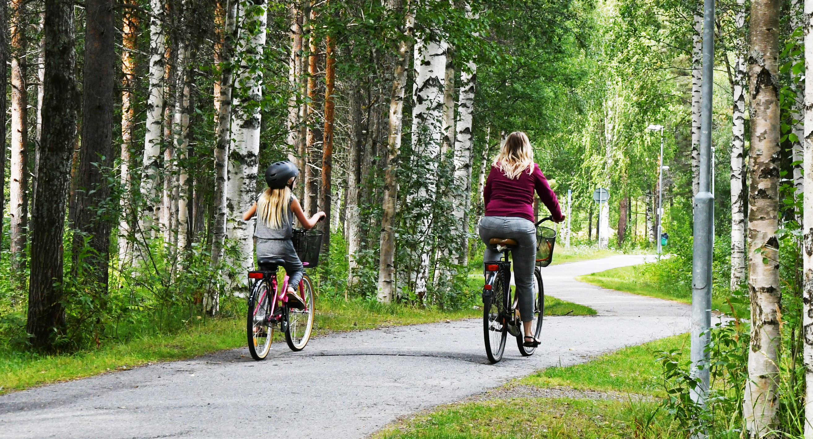 En kvinna och barn cyklar efter en gångstig med ryggen mot kameran. 