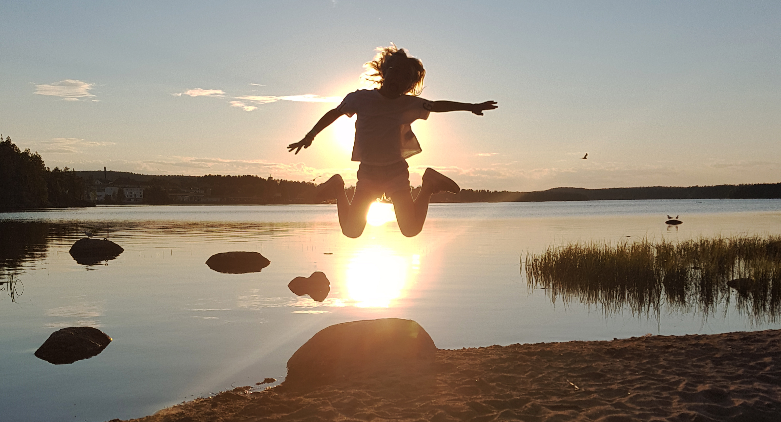 Person i solnedgången hoppar upp i luften vid en sjö. 