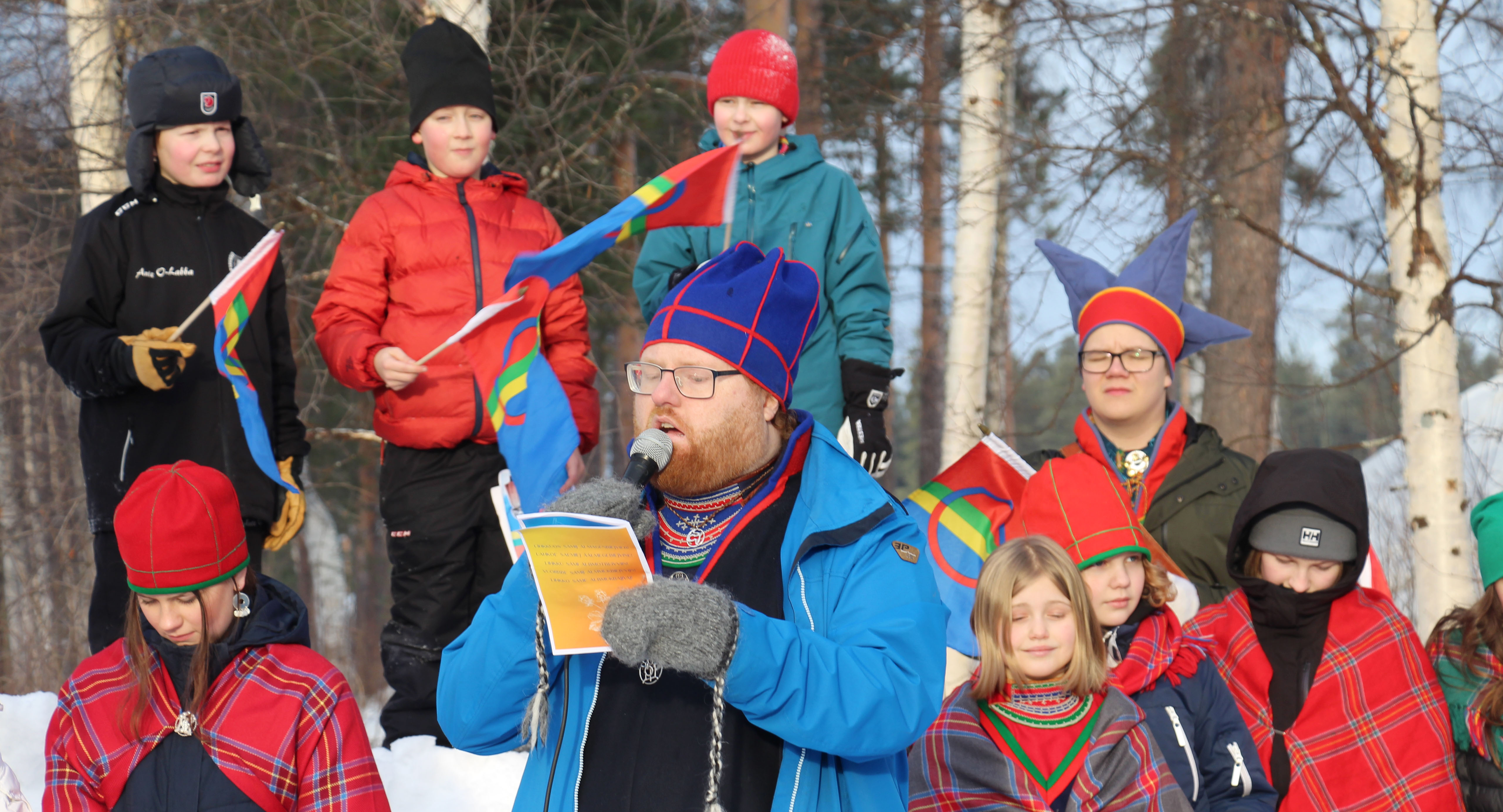 Bild på man som sjunger, samt barn i bakgrunden med samiska dräkter