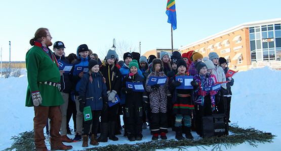 Barn som sjunger samiska nationalsången på en scen gjord av snö på torget i Lycksele. 