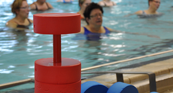 Hantlar att ha till vattengympa i förgrunden och suddig bakgrund med kvinnor i poolen.